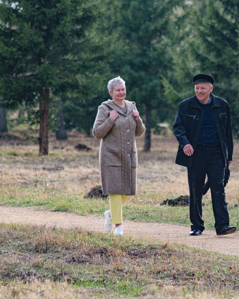 Two residents walking a gravel path through a wooded garden in soft light